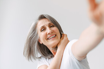 Grey senior woman laughing while reaching her hand to camera