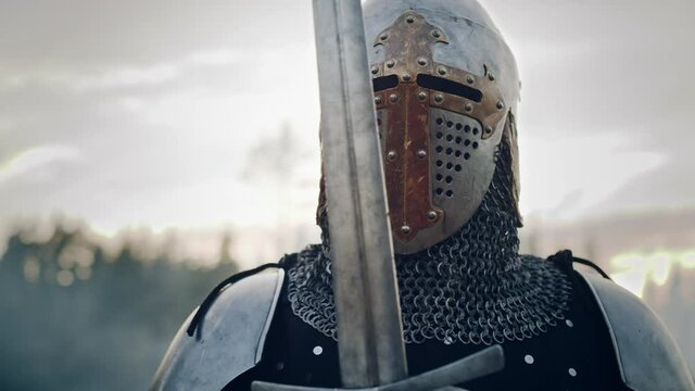 Medieval Knight Wearing Armour and Helmet, Draws Sword from Shearh, Ready to Fight, Kill His Enemy in Battle. Warrior Soldier on Battlefield. War, Invasion, Crusade. Cinematic Historic Reenactment
