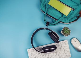 Obraz premium flat lay of headphones, computer keyboard, mouse, school backpack and cactus on blue background with copy space. Online learning concept.