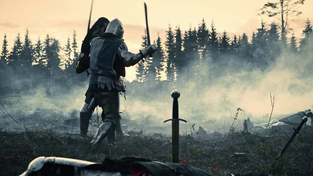 Dark Age Battlefield: Two Armored Medieval Knights Fighting with Swords. Battle of Armed Warrior Soldiers, Killing Enemy in Mysterious Forest. Cinematic Smoke, Mist, Light in Historic Reenactment