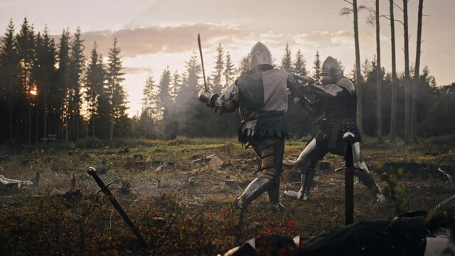 Dark Age Battlefield: Two Armored Medieval Knights Fighting with Swords. Battle of Armed Warrior Soldiers, Killing Enemy in Mysterious Forest. Cinematic Smoke, Mist, Light in Historic Reenactment