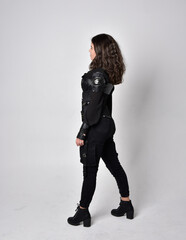 Full length portrait of young woman with natural brown hair,  wearing black leather scifi outfit with corset, standing pose on light grey studio background.