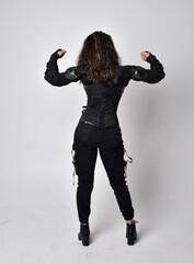 Full length portrait of young woman with natural brown hair,  wearing black leather scifi outfit with corset, standing pose on light grey studio background.
