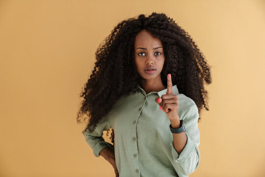 Young black woman with curly hair frowning and showing finger at camera