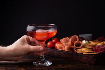 Female hand holding a glass of red liquor and charcuterie board, alcoholic cocktail with a appetizer.