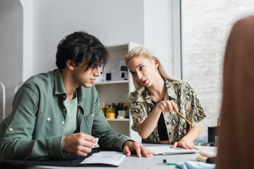 Obraz premium trendy designer pointing with pencil while talking to young tailor in atelier