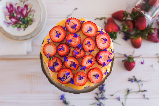 strawberries cut into rounds atop a sponge cake with lemon curd and edible flowers