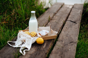 A bottle of milk and a string bag with fruit on wooden boards on the lake
