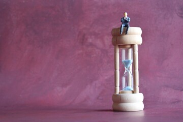 Miniature businessman sitting on hourglass with copy space for text. Productive work and time...
