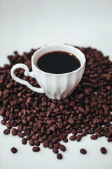 Cup of hot black coffee standing on fresh aromatic roasted coffee beans isolated on white background. Vertical