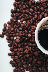 Half of cup of hot coffee standing on fresh aromatic roasted coffee beans isolated on white background