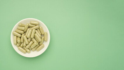Close-up of Andrographis paniculata capsules are in a dish isolated on green background. Space for text. Herbal, medicine, and healthcare concept