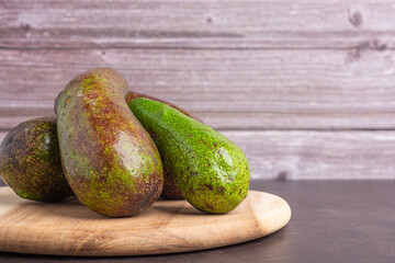 Pile of avocados on a wood cutting board with wooden wall background. Side view. Space for text. Healthy fruits concept
