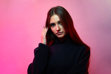 Girl posing in a studio in a trendy neon light. Woman in hoodie with colorful light effects.