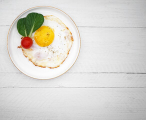 fried egg on a plate with lettuce and tomato on a white wooden background