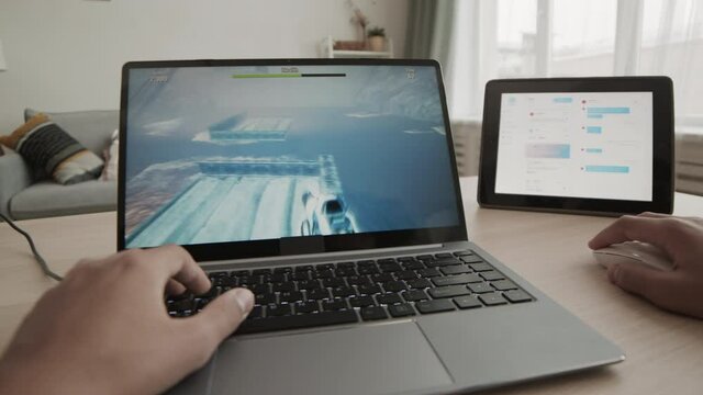 POV of unrecognizable person with hands only in frame sitting at desk in his room, completing quest in game on laptop computer