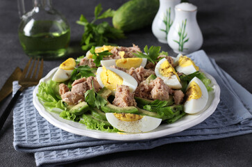 Healthy salad with avocado, tuna, eggs and cucumbers on a white plate on a gray background. Close-up