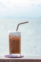 Iced chocolate in a glass on woodtable with sea background
