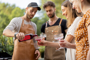 Young people with alcohol drinks at picnic, pouring wine or liqueur into a glasses. image focused on the bottle with blank label to copy paste