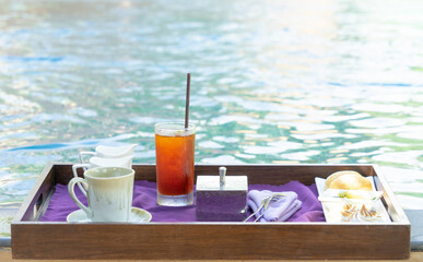 Tea time set with coffee, lemon tea, milk, bread, cookie on white plate with purple napkin near by the swimming pool