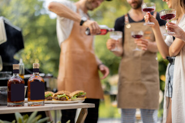 Young people with alcohol drinks at picnic, pouring wine or liqueur into a glasses. Image focused on the bottles at table in front