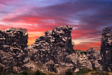 Surrealistic composition of the Devil's Wall near Thale in Saxony-Anhalt, Germany in front of a red and purple evening sky, rib of limestone on the edge of the Harz Mountains