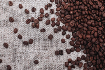 Fresh aromatic roasted coffee beans scattered on a beige burlap background
