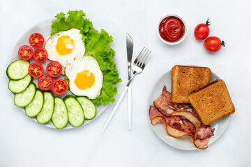 Fried chicken eggs with bacon and vegetables on a gray table. Breakfast concept. Overhead view. Flat lay composition. Food background in morning. Fresh sliced cucumbers and tomatoes with toast.