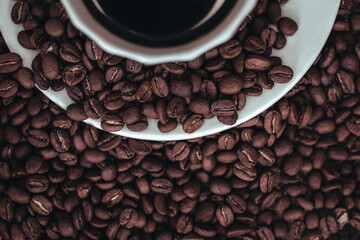 Half of cup of hot black coffee standing on fresh aromatic roasted coffee beans isolated on white background.
