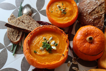 Creamy, nourishing butternut squash soup with a hunk of crusty bread. Fall comfort food. Healthy eating concept. Top view photo of beautiful orange soup served in a squash bowl. 
