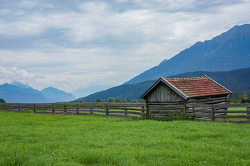 Fototapeta na wymiar wooden cabin and fence with mountains in a background (Mieming area)