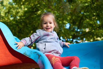 Cute little girl having fun while sliding down a playground slide
