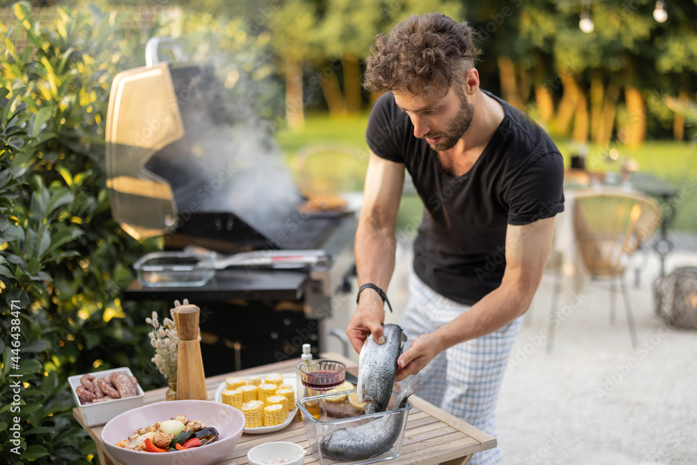 Wall mural men preparing fish for a grill, cooking healthy sea food and vegetables on a modern gas grill at bac