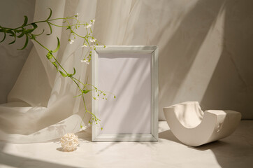 Interior still life with geometric shapes, picture frame with paper sheet, gypsophila flowers. Minimalist gray design mock up. Sunlight and shadows pattern.
