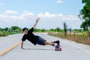 A young Asian man is wearing a black shirt and pants. play skateboard Show the posture of a turn around. On a country road on a sunny day with sky. Looking at the camera, Play surf skate.