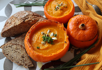 Creamy, nourishing butternut squash soup with a hunk of crusty bread. Fall comfort food. Healthy eating concept. Top view photo of beautiful orange soup served in a squash bowl. 
