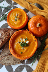 Creamy pumpkin soup and homemade bread on grey tiled table. Soup in a squash top view photo. Thanksgiving menu ideas.  
