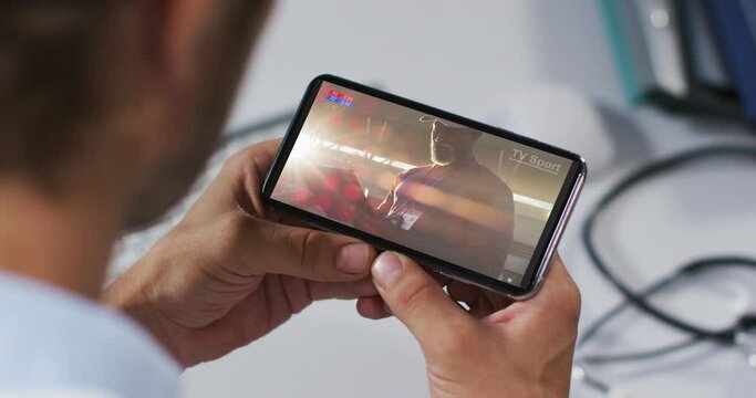 Composite of male doctor watching sports event on smartphone