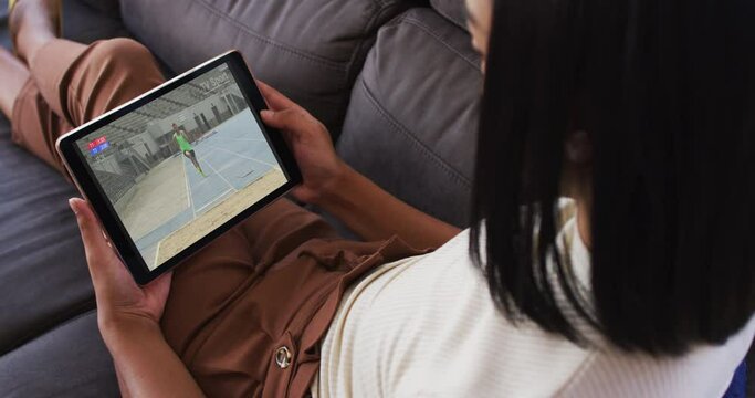 Composite of woman on couch at home watching athletics long jump event on tablet