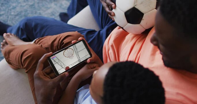 Composite of father and son at home watching basketball game on smartphone