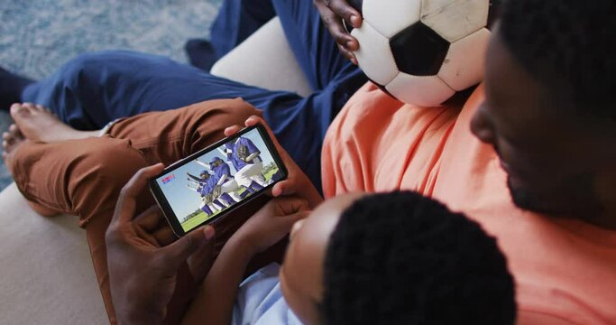 Composite Of Father And Son At Home Watching Baseball Game During Covid 19 On Smartphone