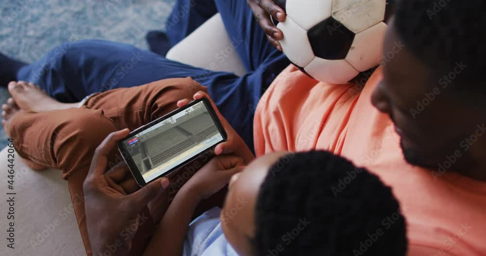 Wall mural Composite of father and son at home watching athletics long jump event on smartphone