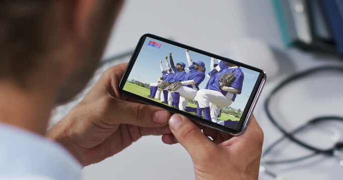 Composite of male doctor watching baseball game during covid 19 on smartphone
