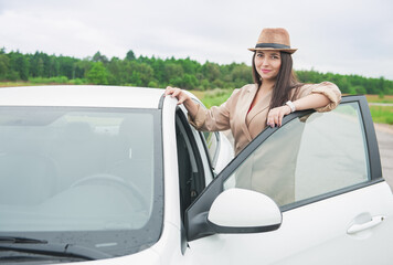Beautiful happy young woman with hat standing near the white car on the road