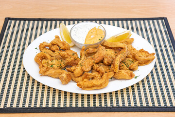 White tray with appetizer of fried breaded chicken strips with chopped parsley, chopped lemons and mayonnaise and mustard sauce for dipping.