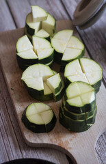 
cutting zucchini with a knife on a wooden cutting board. On the kitchen table