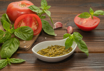 Basil pesto, fresh basil leaves, tomatoes and garlic on wooden background. ingredients for cooking.