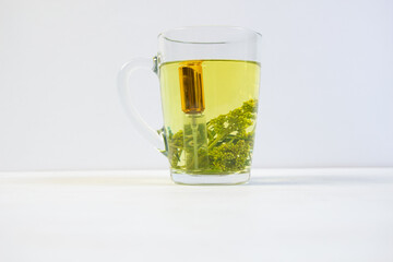 Brewed sagebrush as herbal tea in cup and wormwood essential oil in bottle on white background