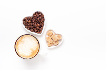 Cup of coffee and heart shaped plates with coffee beans and brown sugar on white background. Top view. Copy space
