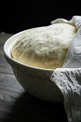 Fresh yeast dough rising in big bowl under white napkin.
